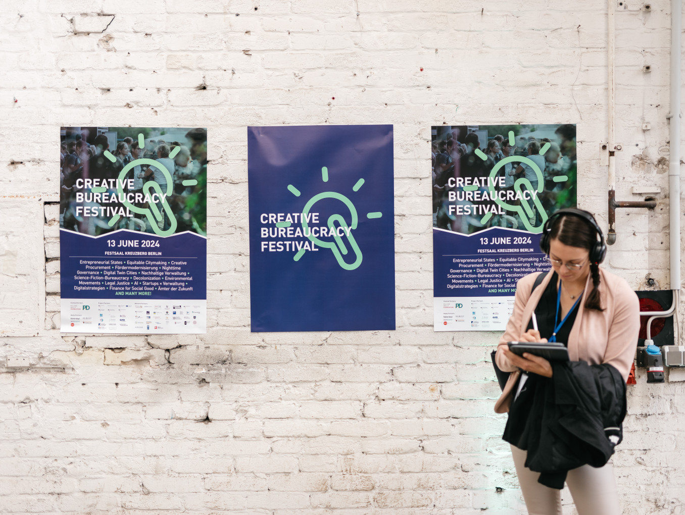 woman with headphones standing infront of three festival posters on the wall