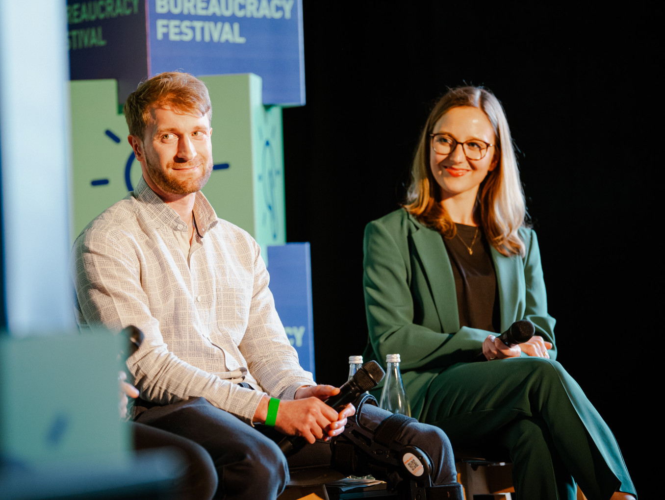 two speaker on stage (men and woman) smiling and listening 