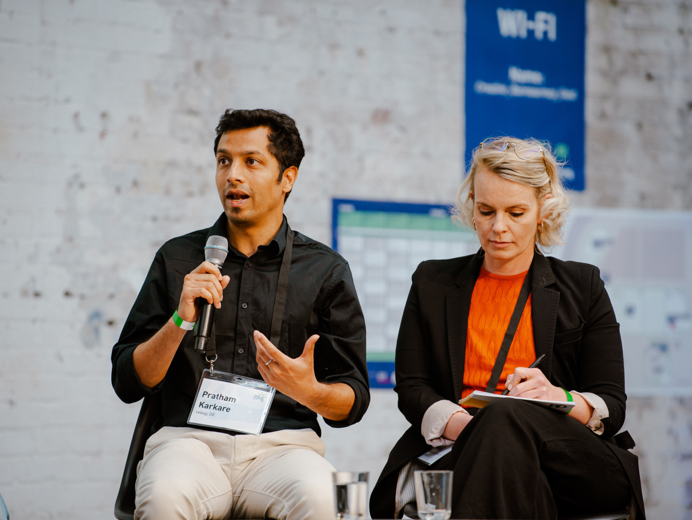 two speakers on stage, men is talking, woman writing something 