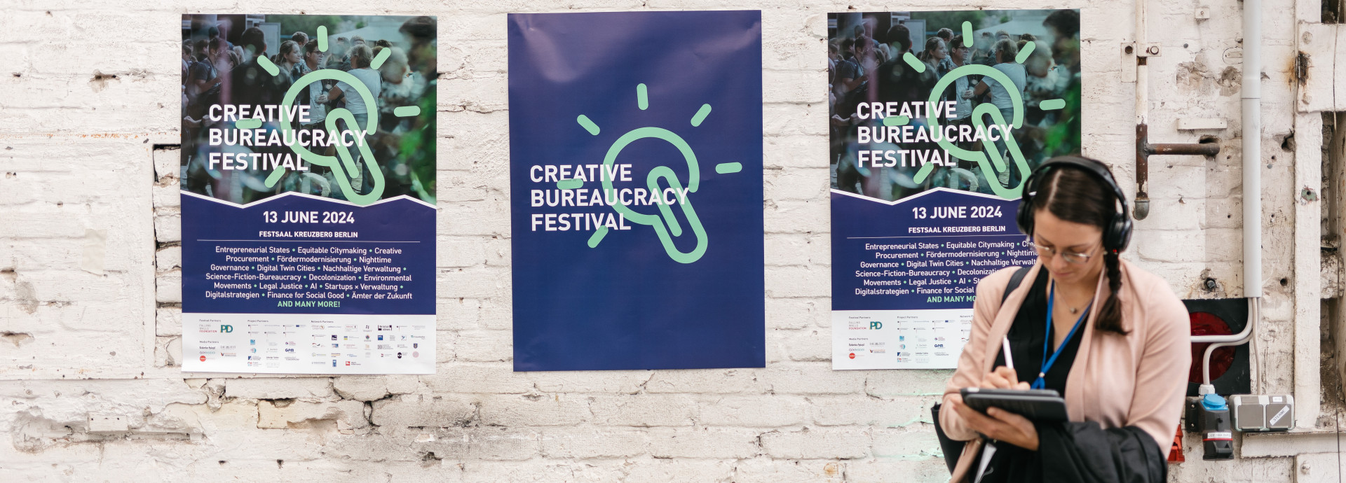 woman with headphones standing infront of three festival posters on the wall