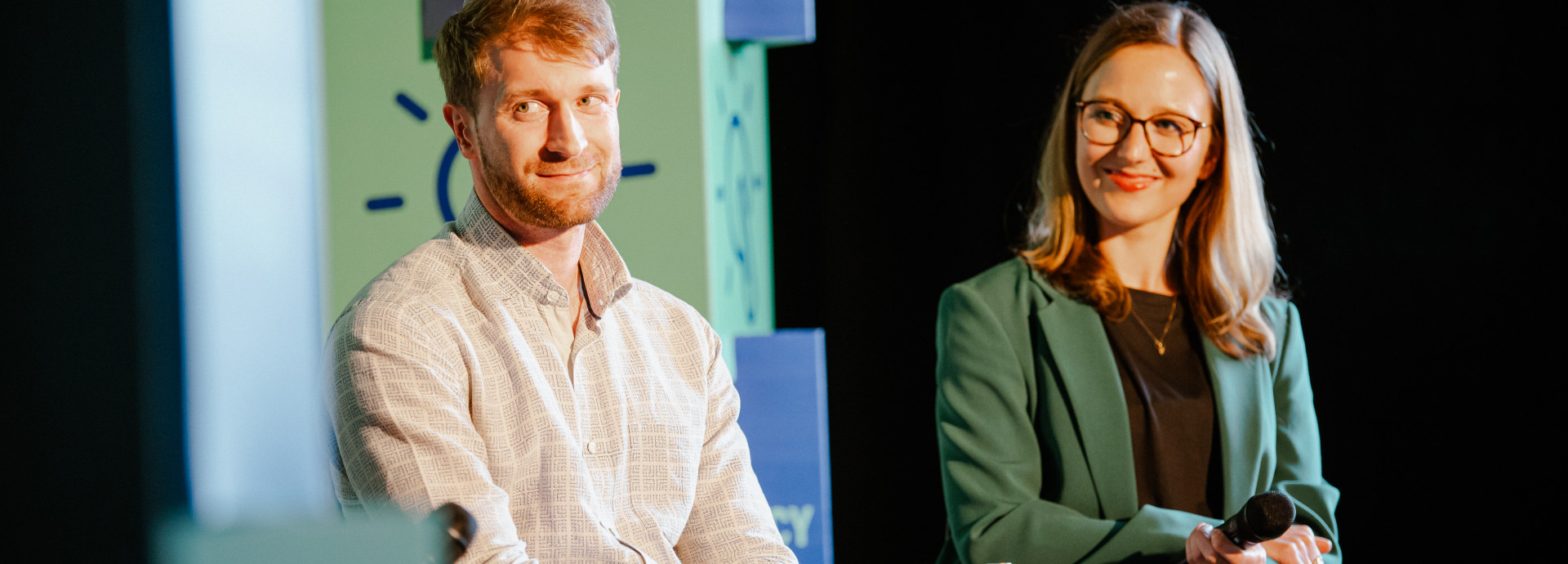 two speaker on stage (men and woman) smiling and listening 