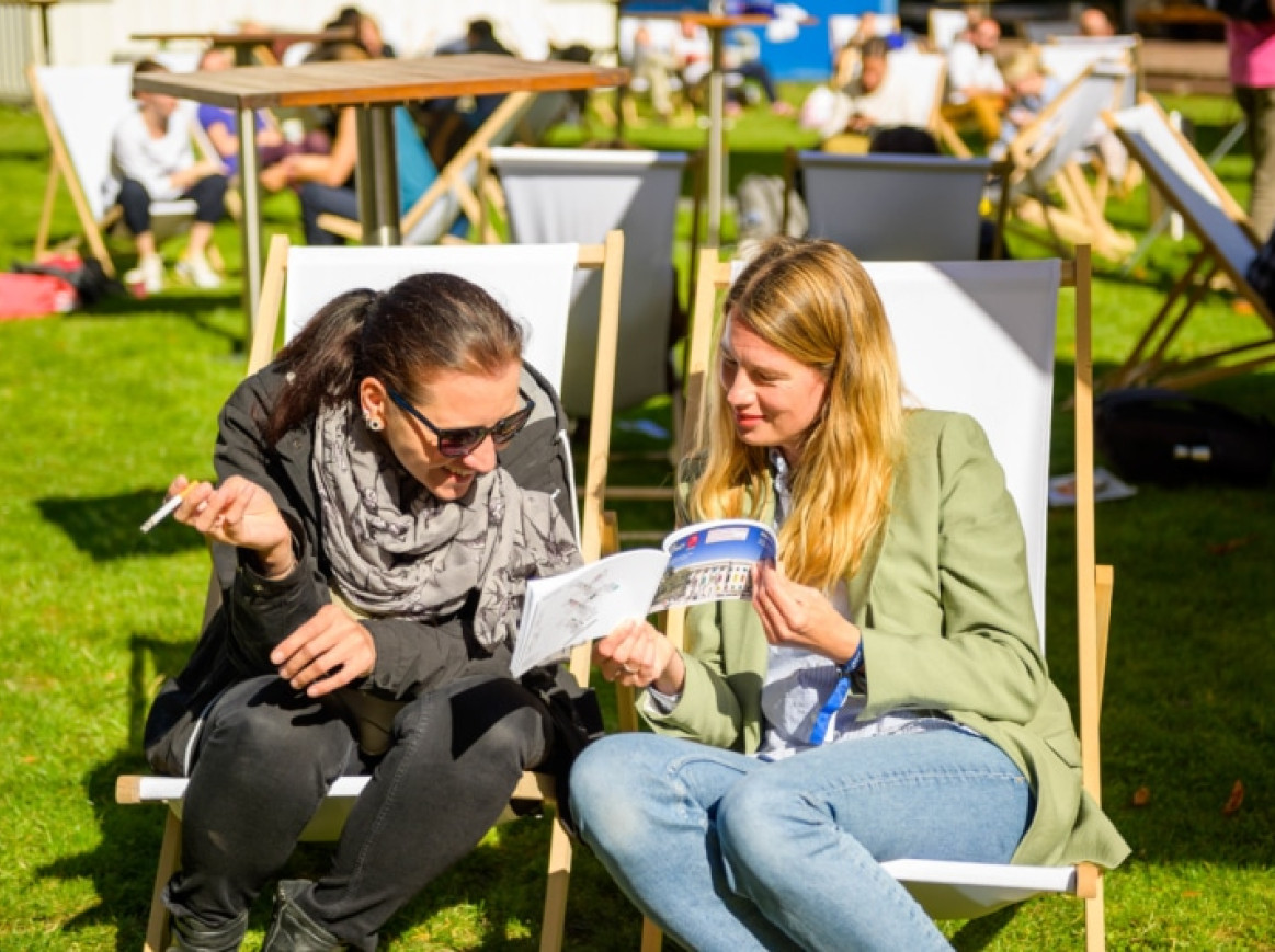 women sitting in the sun in chairs outside looking together at the programme