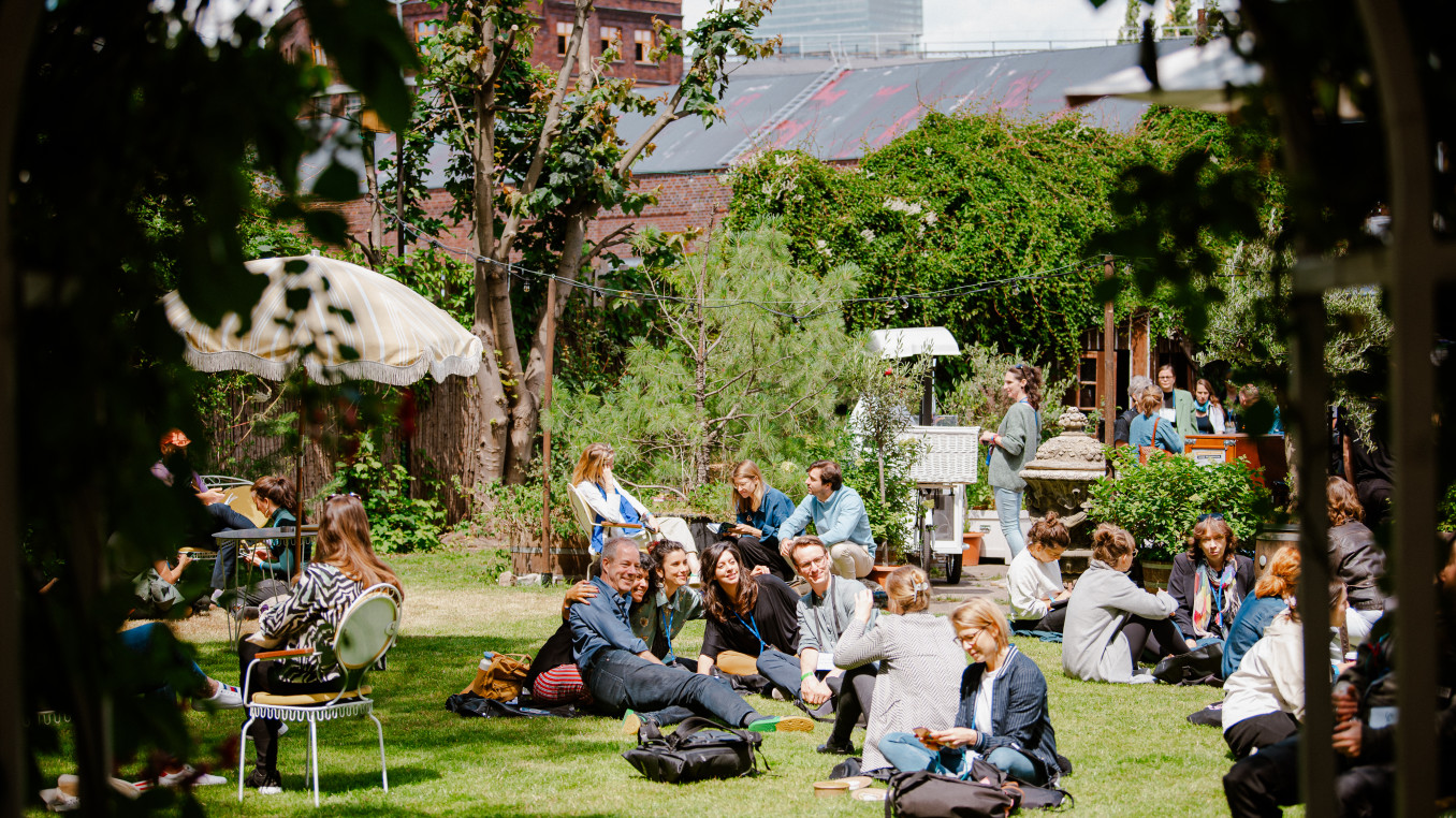 people sitting on the grass at the festival area outside smiling, taking pictures, talking