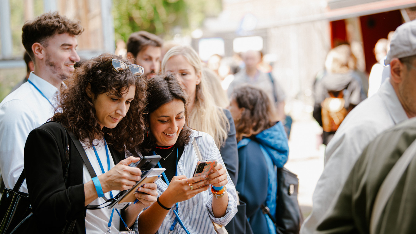 crowd of people and two woman looking smiling on their phones