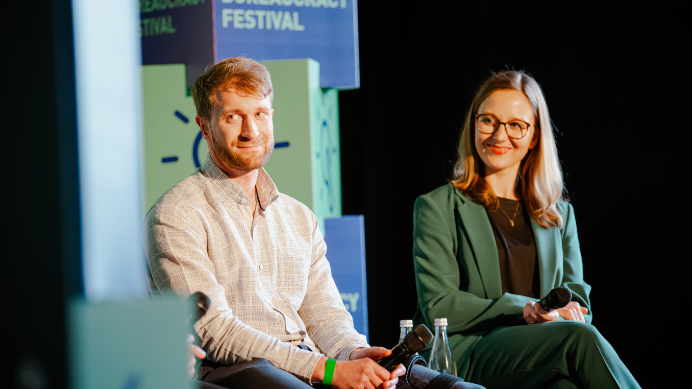 two speaker on stage (men and woman) smiling and listening 