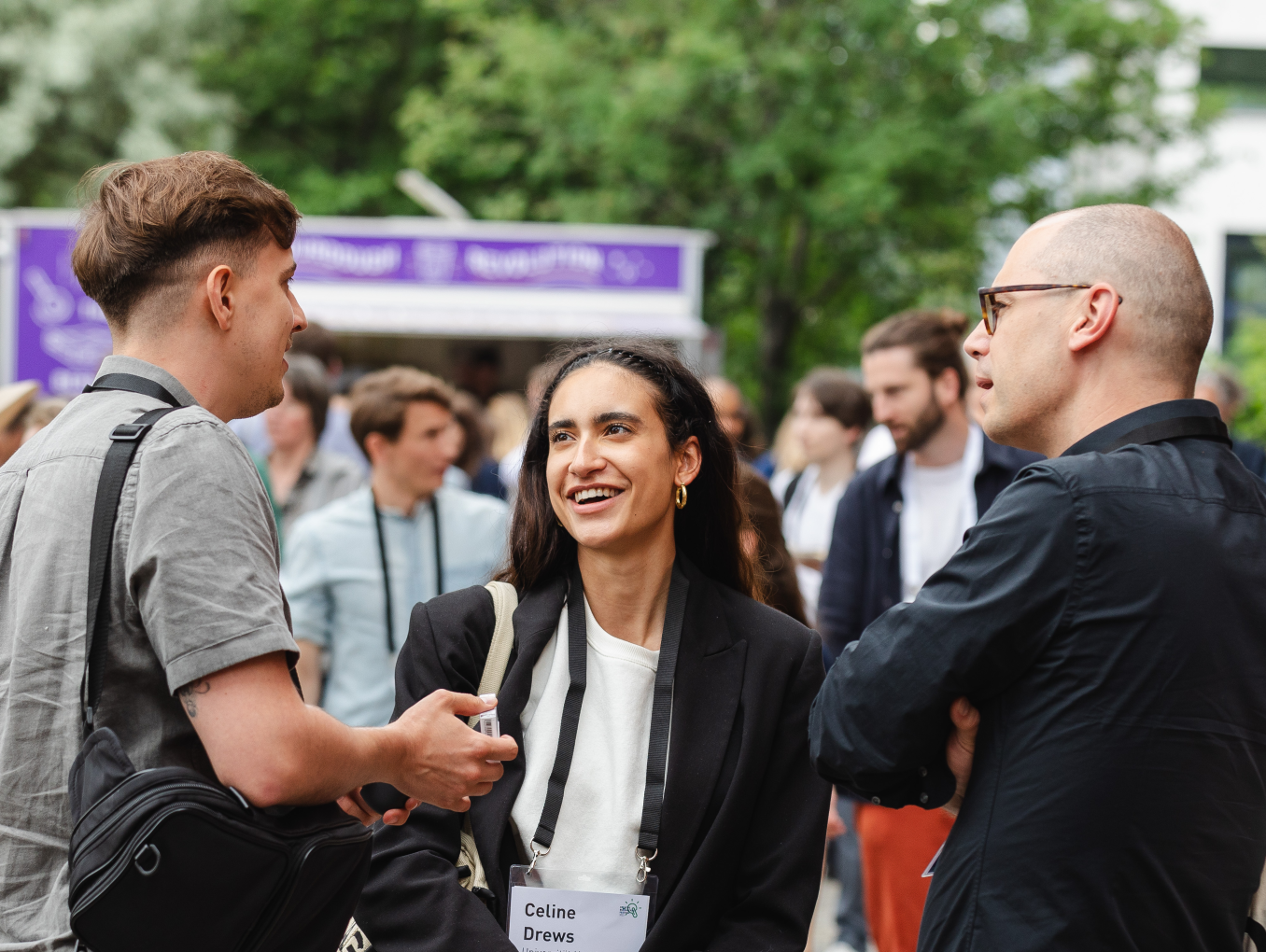 two men and a woman standing at the festival area outside chatting and laughing