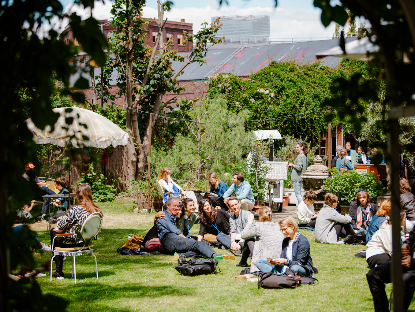 people sitting on the grass at the festival area outside smiling, taking pictures, talking
