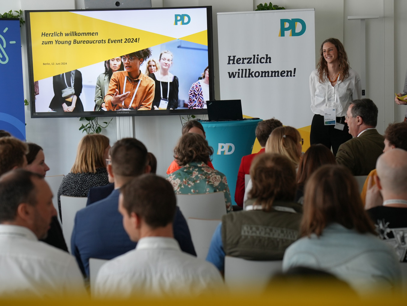 Junge Beamt*innen sitzen im Publikum und hören einer Präsentation zu