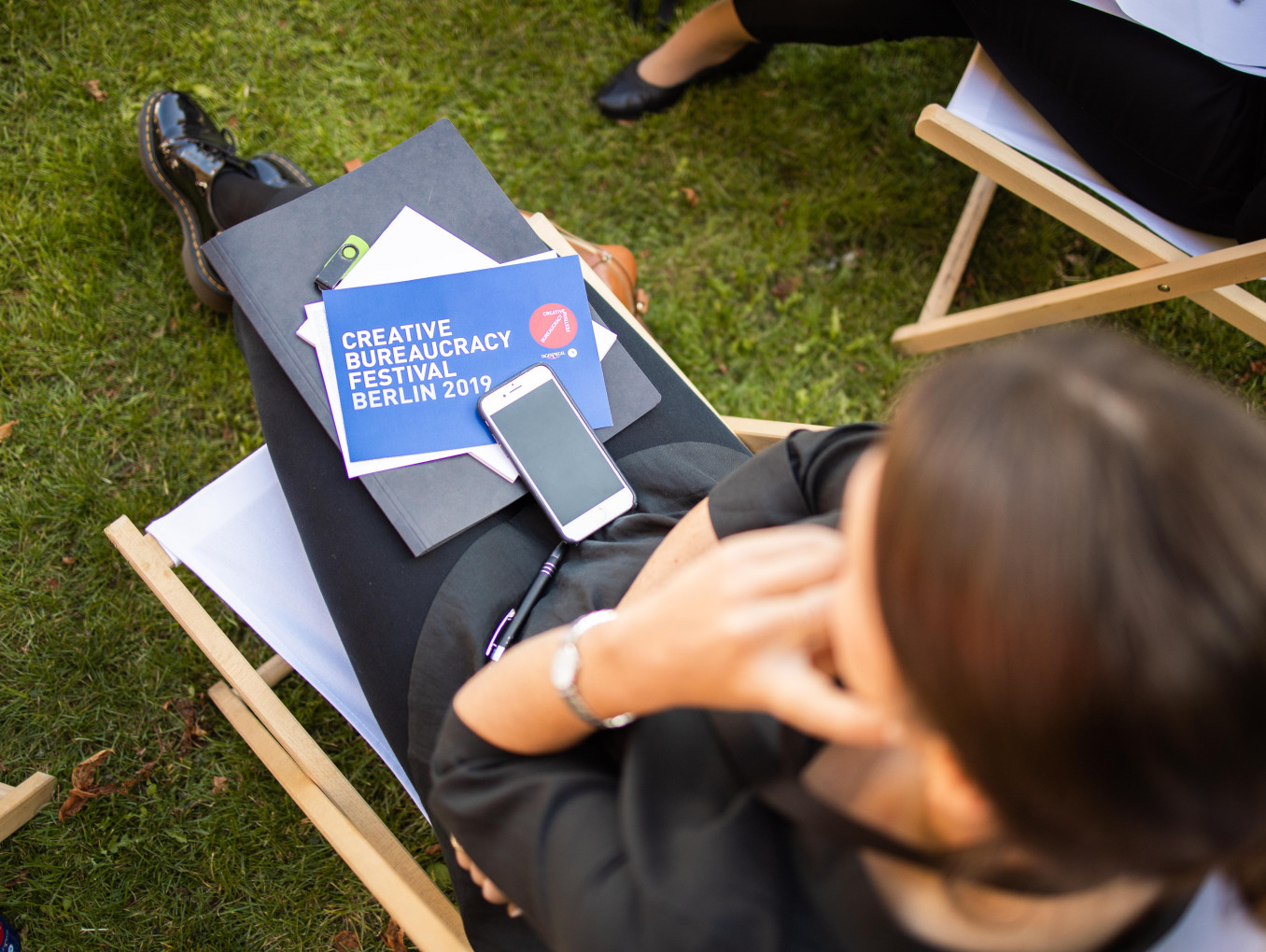 Eine Frau sitzt draußen mit einer Festival-2019-Karte, Papieren und einem Handy auf ihrem Schoß