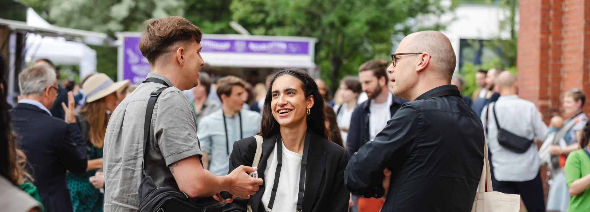 two men and a woman standing at the festival area outside chatting and laughing