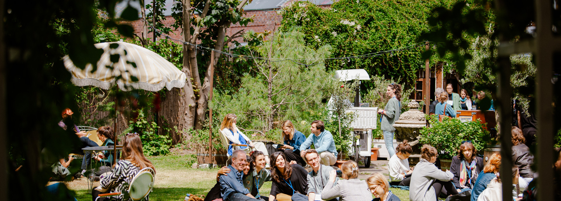 people sitting on the grass at the festival area outside smiling, taking pictures, talking