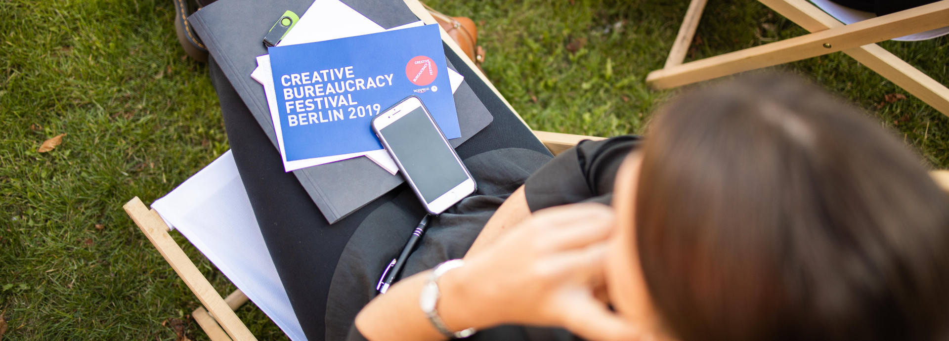 Eine Frau sitzt draußen mit einer Festival-2019-Karte, Papieren und einem Handy auf ihrem Schoß